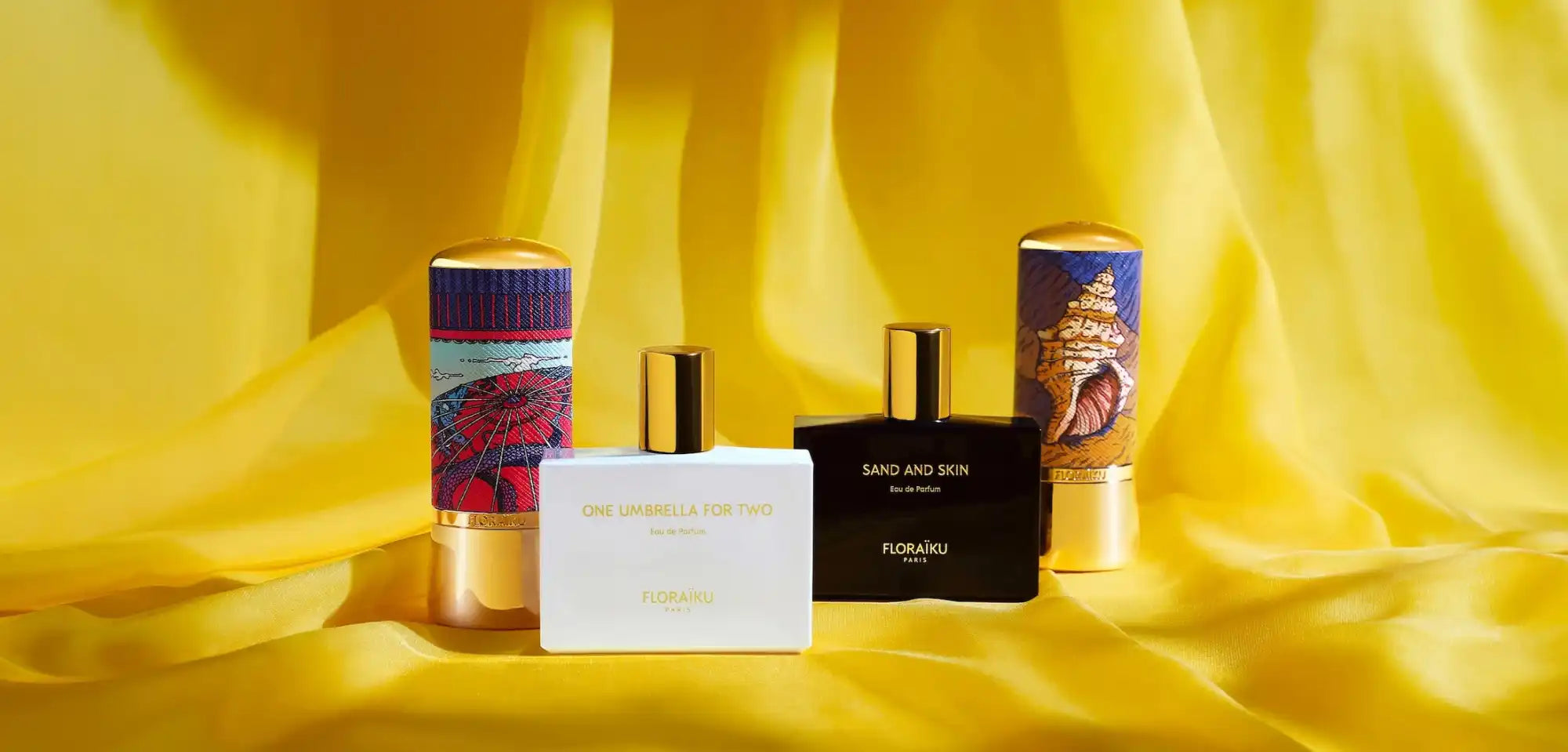 A collection of four perfume bottles, two with decorative sleeves, on a yellow fabric.