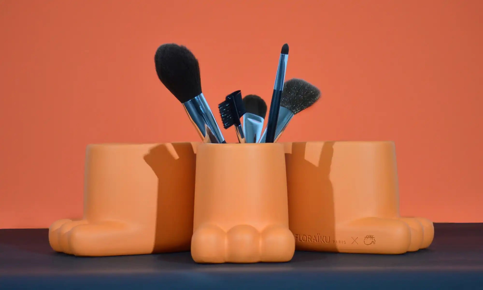 Terracotta-colored ceramic boot or shoe vases holding makeup brushes.
